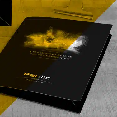 Image noire & blanc avec aplat jaune transparent, présentant une chemise à rabats noire personnalisée avec logo Paulic Meunerie et slogan « Des farines de qualité depuis 4 générations »