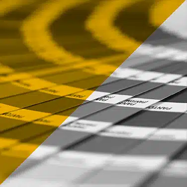 Image noire & blanc avec aplat jaune transparent, gros plan sur un nuancier Pantone en éventail avec bandes colorées et références imprimées