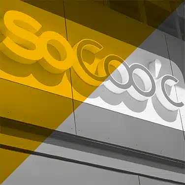 Image en noir & blanc avec aplat jaune en transparence présentant Une enseigne lumineuse SoCoo’c fixée en façade, lettres en relief