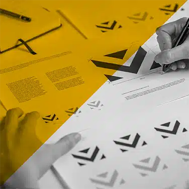 Image noire & blanc avec aplat jaune transparent, gros plan sur un graphiste travaillant sur des planches de logos. Image noir et blanc avec un aplat jaune