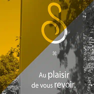 Image en noir & blanc avec aplat jaune en transparence présentant le panneau extérieur avec monogramme stylisée "S" du logo et inscription « Au plaisir de vous revoir »