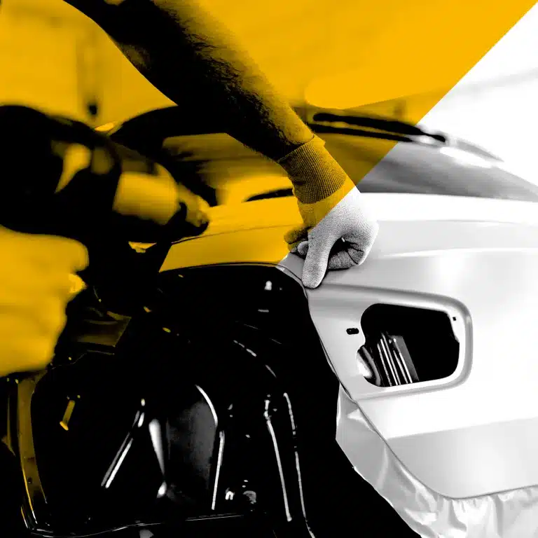 Main d’un technicien posant un adhésif sur un véhicule, gros plan sur la carrosserie, photo N&B avec aplats jaunes — covering véhicule Yescom à Pontivy.